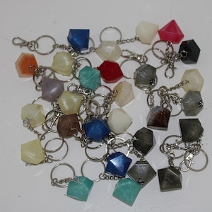 May include: A collection of colorful, geometric resin keychains. Each keychain features a different color and shape, with a silver metal ring and chain.