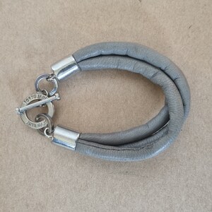 May include: Gray leather bracelet with a silver clasp that says "Tokyo Jeans" on it.