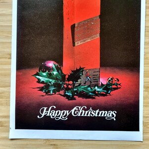 May include: A vintage Christmas advertisement featuring a red bottle, holly, and a purple ornament. The words "Happy Christmas" are written in white script at the bottom. The bottle has a label with text.
