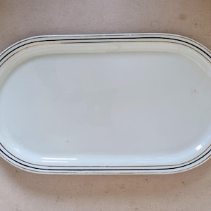 Op de afbeelding: Witte ovale serveerschaal met een zwarte en gouden rand.