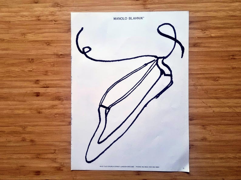 1980s Manolo Blahnik magazine advertisement page showing a bold black line drawing of a pointed-toe shoe with a looping strap on a white background with the Manolo Blahnik name printed at the top.
