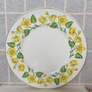 Puede incluir: Un plato de cena de cerámica blanca con un borde dorado y un borde de flores amarillas con hojas verdes.