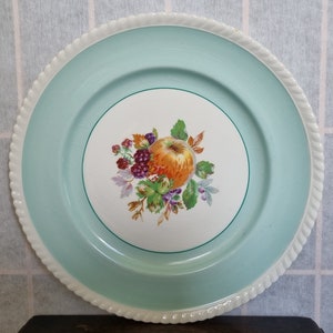 Puede incluir: Un plato de cena vintage de cerámica, azul claro y blanco, con un borde elevado y un diseño floral con una manzana y bayas.