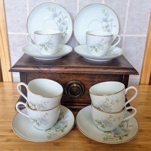May include: Set of six white teacups and saucers with a floral design. The cups and saucers have a gold trim. The cups and saucers are arranged in two stacks of three.
