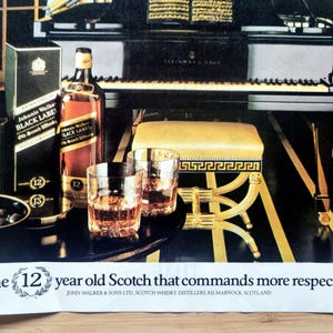 May include: An advertisement featuring a bottle and box of Johnnie Walker Black Label Scotch whisky, two glasses of amber liquid, and a piano. The text reads "The 12 year old Scotch that commands more respect."
