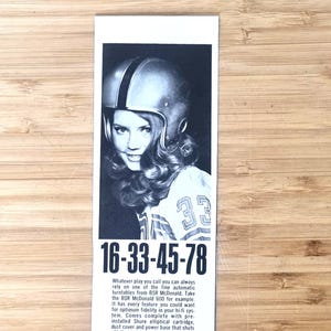 May include: Black and white vintage advertisement featuring a woman wearing a football helmet and jersey with the number 33. The ad includes the numbers 16-33-45-78 and text promoting BSR McDonald turntables.