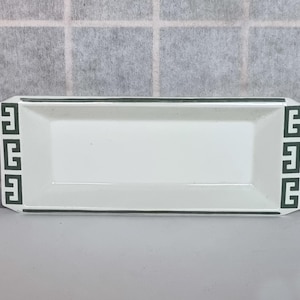 May include: A rectangular white ceramic tray with a dark green geometric border design. The tray has a simple, elegant design, suitable for serving or display. The tray's dimensions are approximately 12 inches long and 6 inches wide.