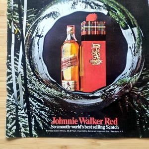 Puede incluir: Un anuncio de whisky escoc&eacute;s Johnnie Walker Red. La imagen presenta una botella de whisky y una caja de regalo roja con un patr&oacute;n de tart&aacute;n. El texto dice: "Johnnie Walker Red, So smooth-world's best selling Scotch."