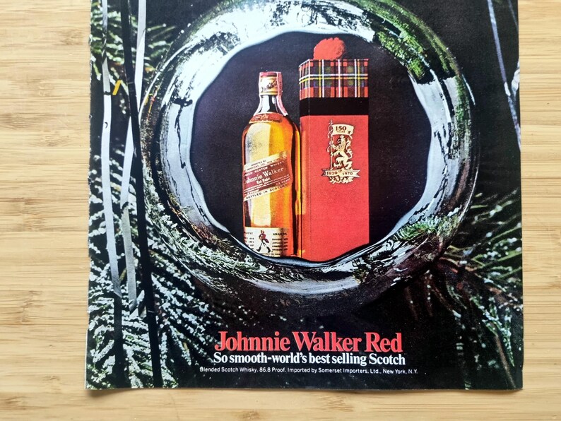 Puede incluir: Un anuncio de whisky escoc&eacute;s Johnnie Walker Red. La imagen presenta una botella de whisky y una caja de regalo roja con un patr&oacute;n de tart&aacute;n. El texto dice: "Johnnie Walker Red, So smooth-world's best selling Scotch."