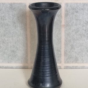 May include: A small, dark blue ceramic vase with a flared top and bottom. The vase has a smooth, glossy finish.