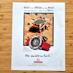 Może przedstawiać: Reklama zegarka Omega z czerwonym paskiem. Reklama zawiera tekst "NASA took OMEGA to the Moon" i "Also available on Earth!" ze zdjęciem łazika marsjańskiego.