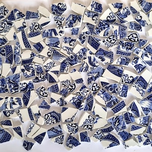 May include: A collection of broken ceramic pieces with a blue and white floral pattern. The fragments vary in size and shape, scattered across a white surface. The design appears to be a classic blue and white porcelain style.