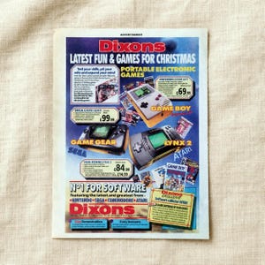 May include: A vintage Dixons advertisement for portable electronic games featuring a Nintendo Game Boy, Sega Game Gear, and Atari Lynx 2. The colorful print includes text detailing various gaming consoles, software offers, and prices in British pounds.