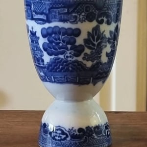 May include: Blue and white porcelain egg cup with a traditional Chinese pattern. The cup has a wide base and a narrow top.