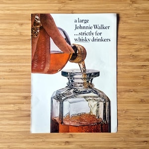 Original 1960s Johnnie Walker magazine advertisement showing whisky being poured into a clear glass decanter, with bold minimalist headline text. Authentic vintage Scotch whisky print with rich amber tones, clean typography, and light age-related wear visible along the edges.