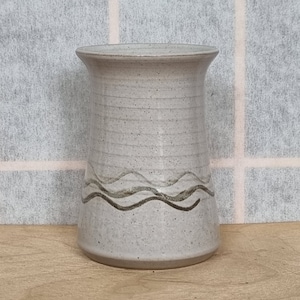 Puede incluir: Un jarrón de cerámica blanco con un diseño ondulado marrón alrededor del medio.