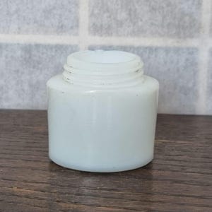 May include: A white opaque glass jar with a smooth, rounded surface. The jar is empty and has a wide mouth opening.