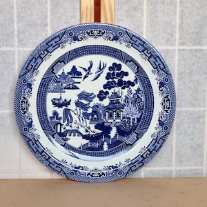 May include: A blue and white ceramic plate with a traditional willow pattern design. The plate features a central image of a pagoda, trees, and birds.