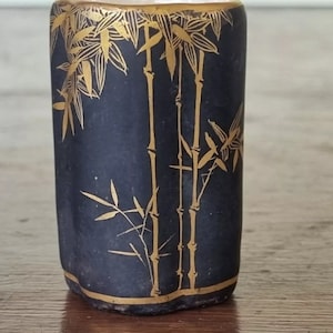 May include: A small, black ceramic vase with a gold bamboo design. The vase has a hexagonal shape and a slightly flared lip.