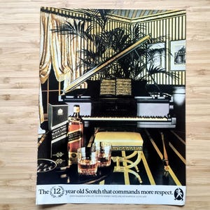 Vintage Johnnie Walker Black Label 12-year Scotch ad with bottle and glasses in an elegant room featuring a grand piano; approx 10 × 7 inches.