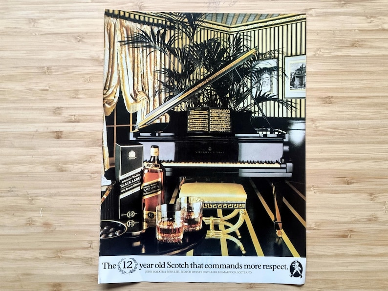 Vintage Johnnie Walker Black Label 12-year Scotch ad with bottle and glasses in an elegant room featuring a grand piano; approx 10 × 7 inches.