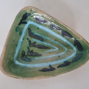 Könnte beinhalten: Eine dreieckige Keramikschale mit grüner Glasur und einem weißen und blauen Design. Die Schale hat eine einzigartige Form und ein handgemaltes Design.