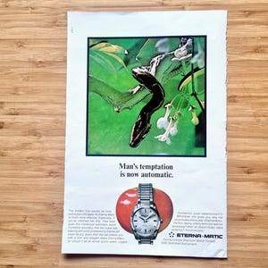 May include: Vintage advertisement featuring a silver wristwatch with a metal band, set against a red apple. The ad includes a green and white illustration of a snake and flowers, with the text "Man's temptation is now automatic."