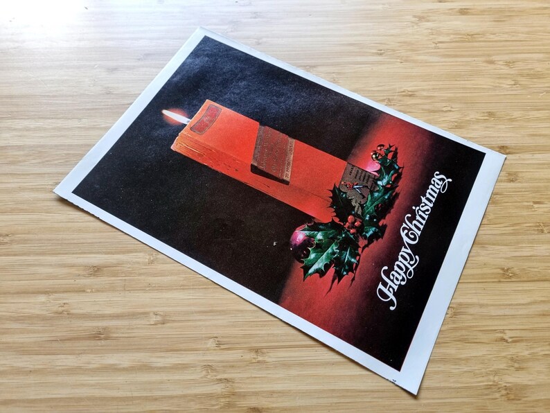 May include: A vintage Christmas card depicting a red candle with a lit flame, a sprig of holly, and the words "Happy Christmas" in white script. The background fades from black to red.