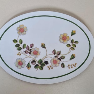 Può includere: Sottopentola ovale in ceramica bianca con bordo verde e un motivo floreale con fiori bianchi e gialli con foglie verdi.