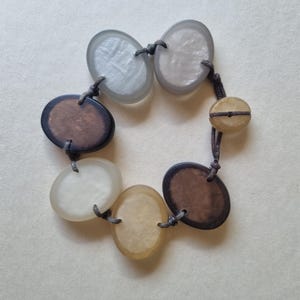 May include: A bracelet made of brown and white oval-shaped beads connected by a brown cord.