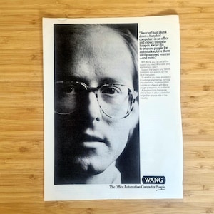 May include: Black and white advertisement featuring a man wearing glasses. The ad includes text about preparing people for automation and the company name "WANG" with the tagline "The Office Automation Computer People."