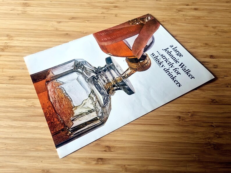 May include: Vintage advertisement for Johnnie Walker whisky. The image features a detailed illustration of a whisky bottle and a glass being filled. The text reads "a large Johnnie Walker...strictly for whisky drinkers."