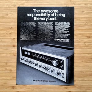 以下が含まれることがあります： Pioneer SX-828 AM-FMステレオレシーバーの広告。広告には「最高の責任を負う」というテキストが表示されています。レシーバーはシルバーとブラックで、複数のノブとダイヤルが付いています。