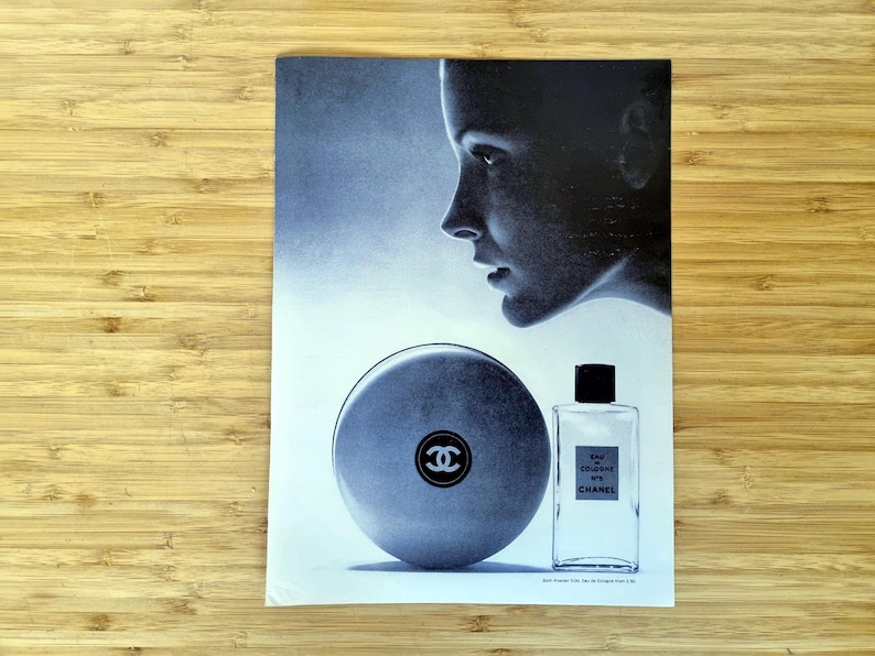 Original 1960s Chanel No. 5 magazine advertisement showing a minimalist composition with a softly lit female profile alongside the iconic round bath powder container and rectangular perfume bottle. A refined black-and-white luxury beauty image reflecting mid-century French fashion and fragrance advertising.