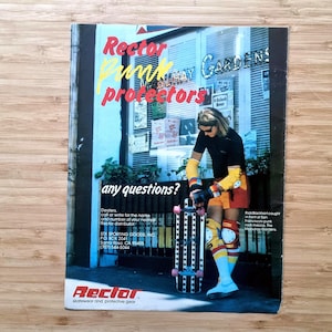 May include: An advertisement for Rector skatewear and protective gear. The image features a person wearing protective gear, holding a skateboard. The ad includes the text "Rector" and "Protectors". The background shows a storefront with the text "Mahoney Gardens".