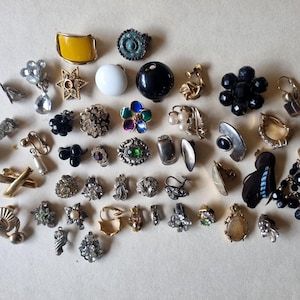 Puede incluir: Una colección de pendientes vintage en varios estilos y colores. Los pendientes incluyen de clip, de botón y colgantes. Los colores incluyen dorado, plateado, negro, blanco, amarillo y turquesa. Algunos pendientes presentan pedrería, perlas y otros elementos decorativos.