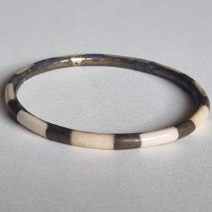 Op de afbeelding: Een gouden armband met een wit en zwart geruit patroon.