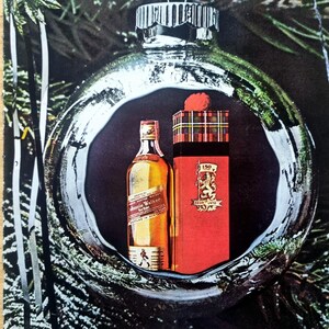 Puede incluir: Un anuncio con una botella de whisky Johnnie Walker y una caja de regalo roja con un patr&oacute;n de cuadros, dentro de una gran bola de Navidad plateada. La caja de regalo tiene un escudo y el texto "150 1820-1970". El fondo incluye ramas de hoja perenne.