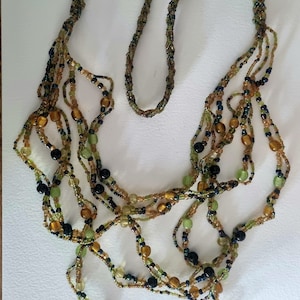 May include: A multi-strand necklace made of small, colorful beads. The beads are in shades of green, brown, and black. The necklace is layered and has a cascading effect.