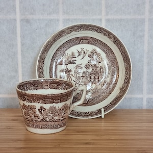 May include: A brown and white teacup and saucer with a willow pattern design. The cup and saucer are made of ceramic and have a traditional look.