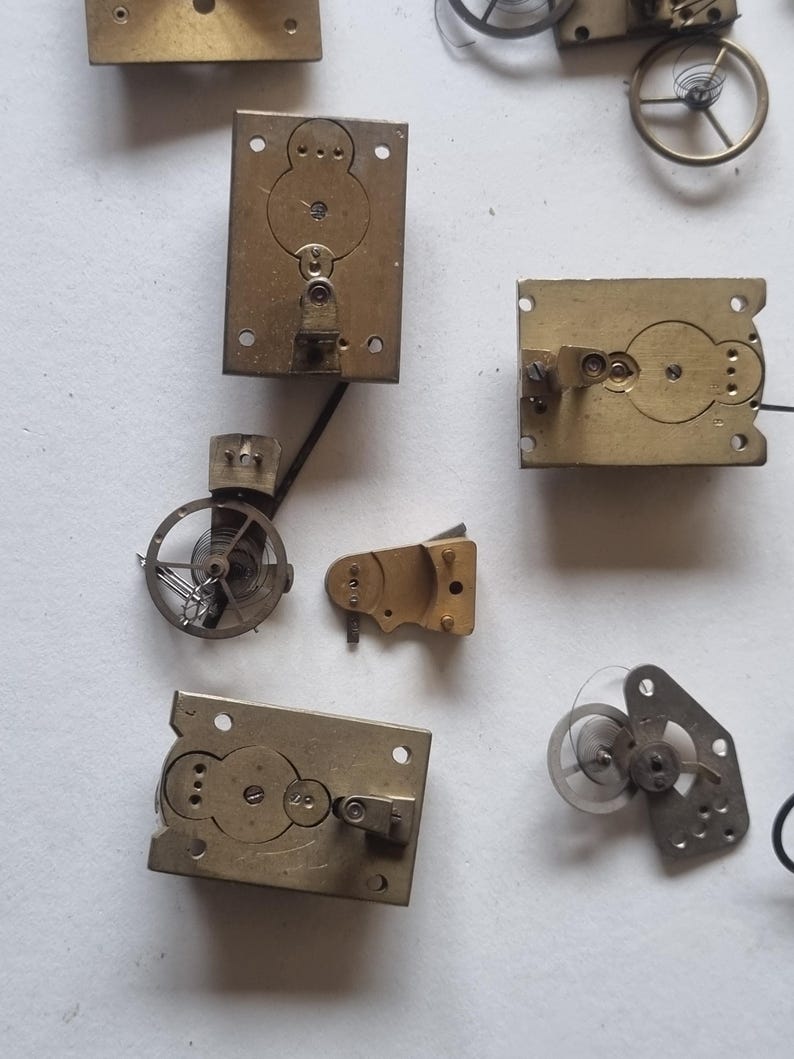 May include: A collection of vintage watch parts, including brass plates, gears, and springs. The components are in various shapes and sizes, with intricate details visible. The image showcases the mechanical elements of timekeeping devices.
