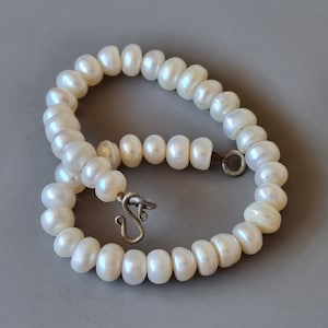 Puede incluir: Un collar de perlas blancas con un cierre de plata. El collar está hecho de pequeñas perlas redondas.