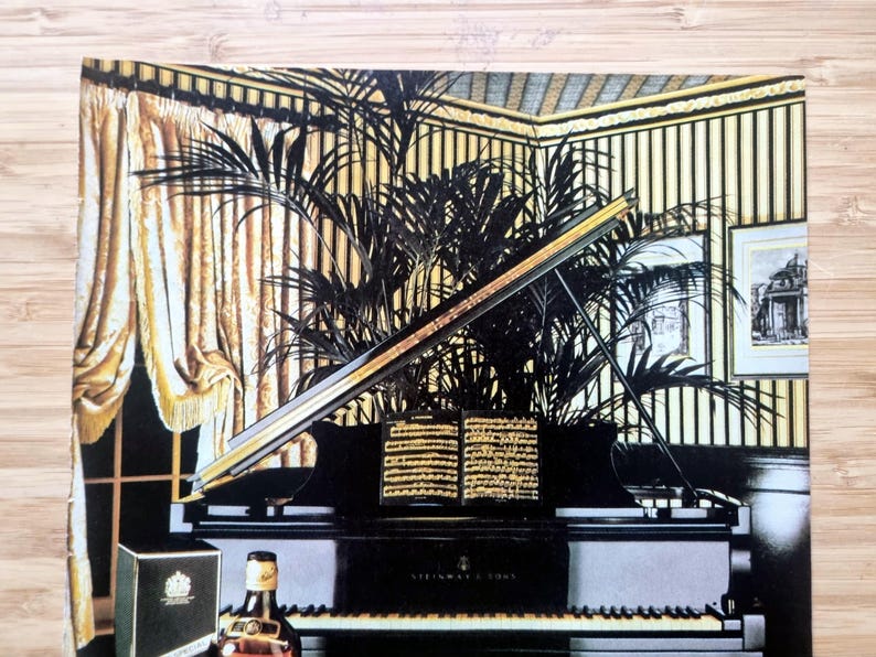 May include: An illustration of a grand piano with a black finish, open to reveal sheet music. A bottle of liquor and a box are in the foreground. The background features a room with gold curtains, striped wallpaper, and framed artwork.
