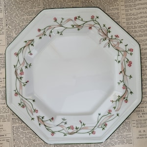 Puede incluir: Un plato octogonal blanco con un borde verde y un diseño floral con flores rosas, hojas verdes y cintas blancas.