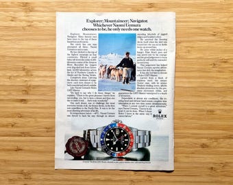May include: An advertisement featuring a Rolex GMT-Master watch with a black dial and a red and blue bezel. The ad includes a photo of a man with sled dogs in a snowy landscape. The text reads "Explorer; Mountaineer; Navigator."