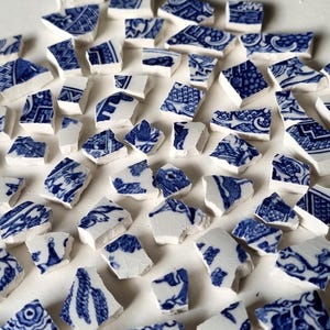 May include: A white ceramic mug with a black handle and the text "But First, Coffee" in a bold, black font. The mug is set against a blurred background, suggesting a cozy setting.