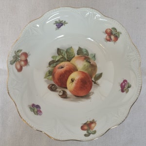 May include: A white porcelain bowl with a gold rim and a hand-painted design of apples, nuts, and berries. The bowl has a scalloped edge and is decorated with a delicate floral pattern.