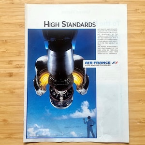 May include: An advertisement for Air France featuring a jet engine against a blue sky background. The ad includes the text "High Standards" and "Air France, We're aiming even higher."