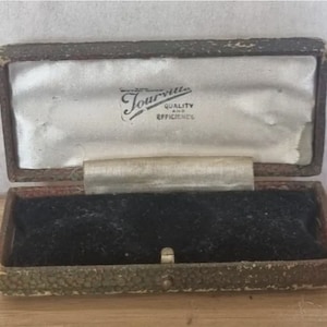 May include: A vintage, brown, rectangular jewelry box with a black velvet interior. The box is open and the lid has a white label with the text "Tourville Quality and Efficiency".