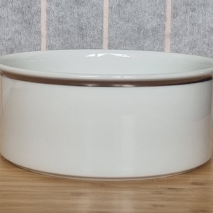 Könnte beinhalten: Eine weiße Keramikschüssel mit leicht abgerundetem Rand. Die Schüssel ist glatt und hat eine glänzende Oberfläche.